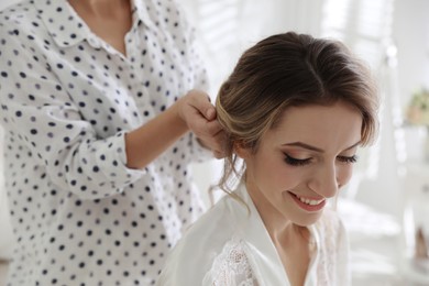 Photo of Professional stylist making wedding hairstyle for bride in salon