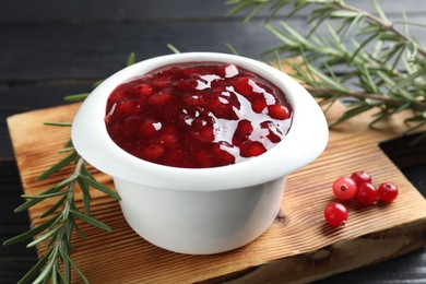 Photo of Cranberry sauce in bowl, fresh berries and rosemary on table, closeup
