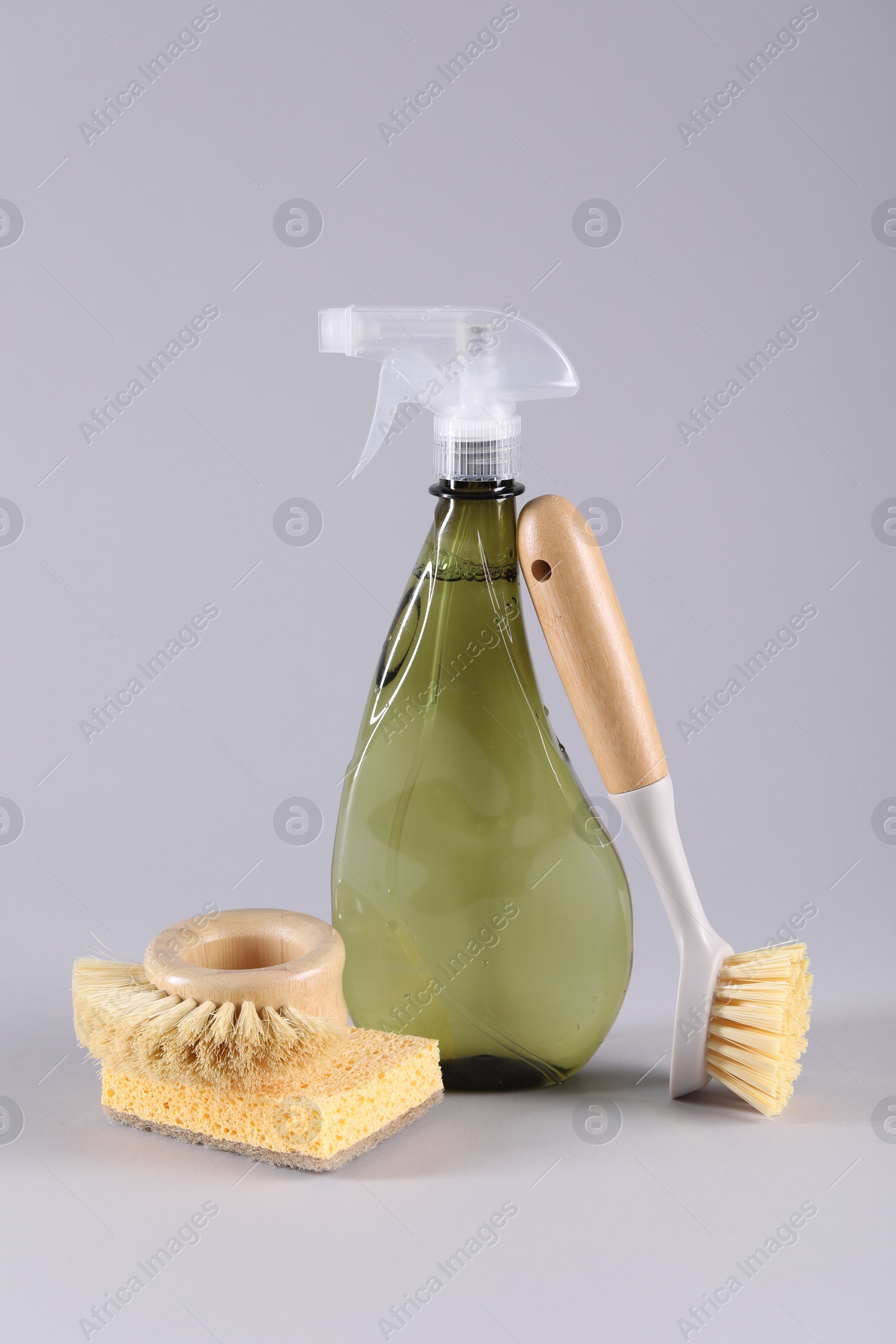 Photo of Bottle of cleaning product, sponge and brushes on light grey background