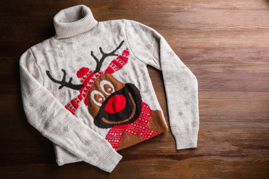 Warm Christmas sweater with deer on wooden table, top view