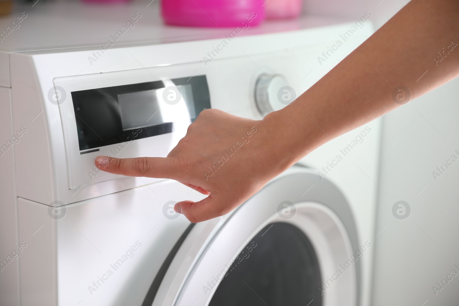 Photo of Woman pressing button on washing machine in bathroom, closeup