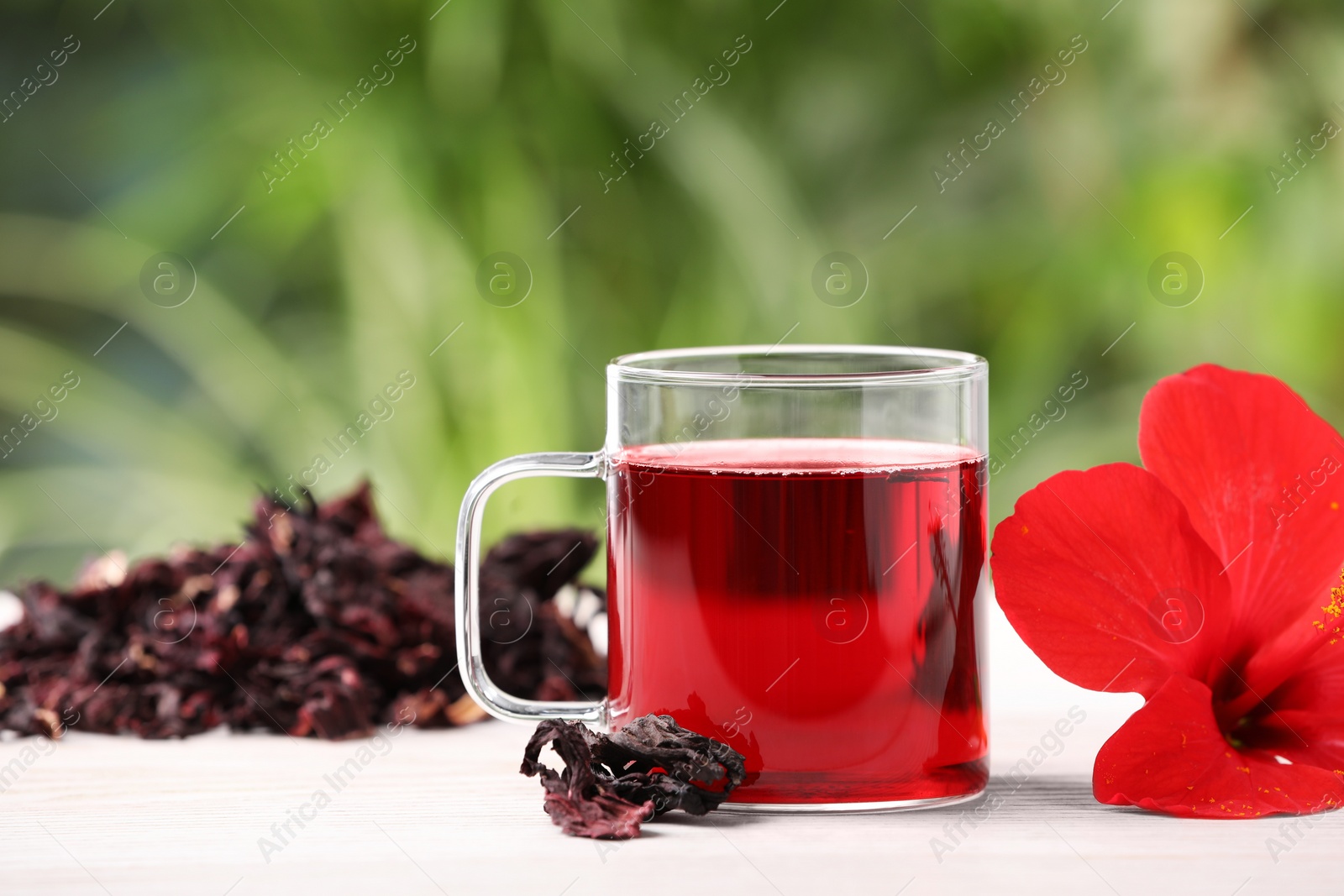 Photo of Delicious hibiscus tea and flowers on white wooden table outdoors, closeup