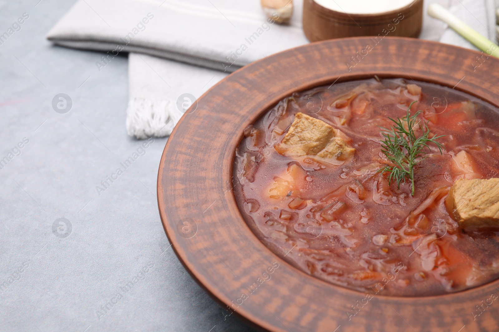 Photo of Bowl of delicious borscht on light grey table, closeup. Space for text