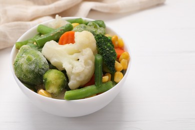 Photo of Mix of different frozen vegetables in bowl on white wooden table, closeup/ Space for text