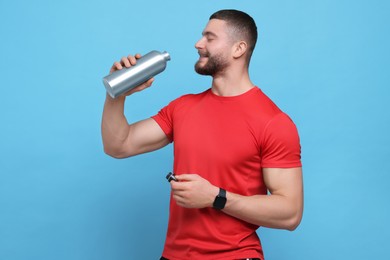 Photo of Handsome man with thermo bottle on light blue background, space for text