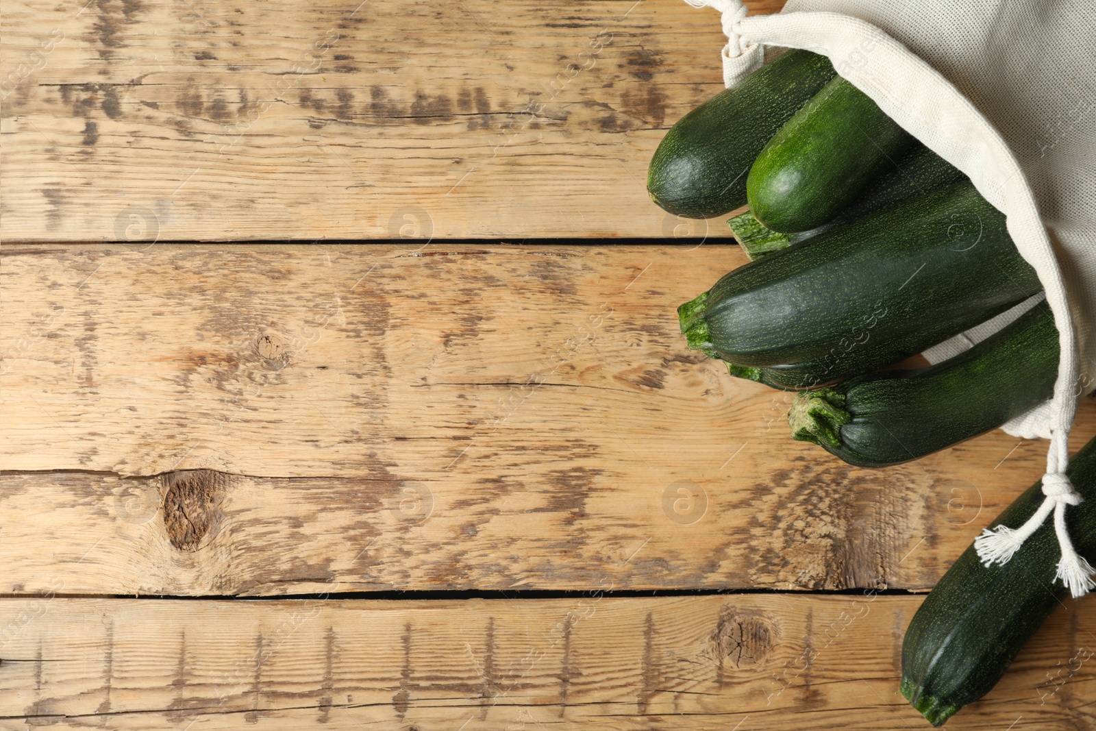 Photo of Sack with green ripe zucchinis on wooden table, flat lay. Space for text