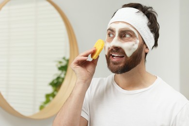 Photo of Man with headband washing his face using sponge in bathroom, space for text