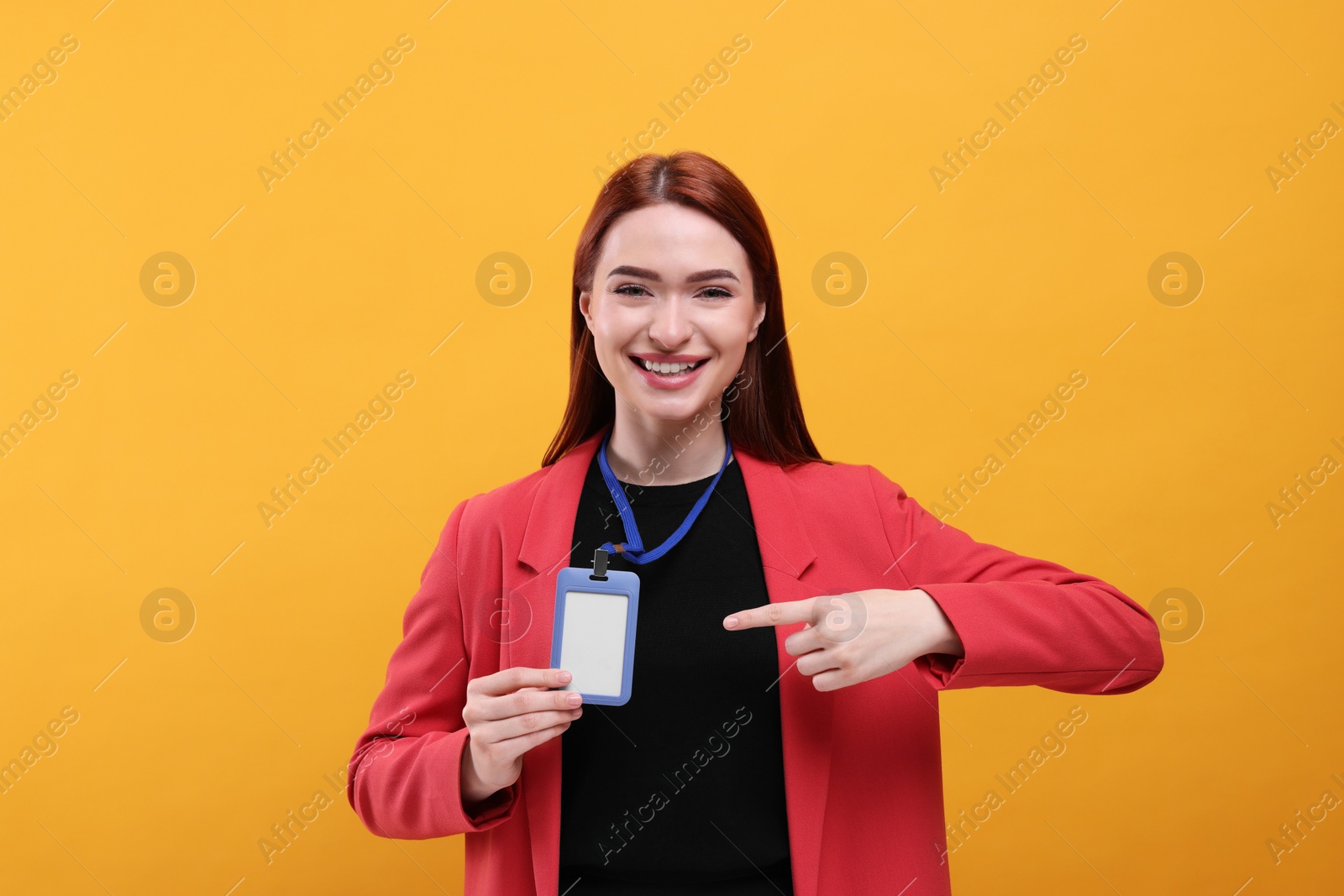 Photo of Smiling woman pointing at vip pass badge on orange background