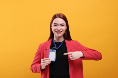 Photo of Smiling woman pointing at vip pass badge on orange background