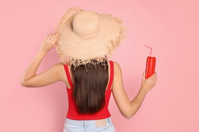Photo of Young woman in straw hat holding tin can with beverage on pink background, back view