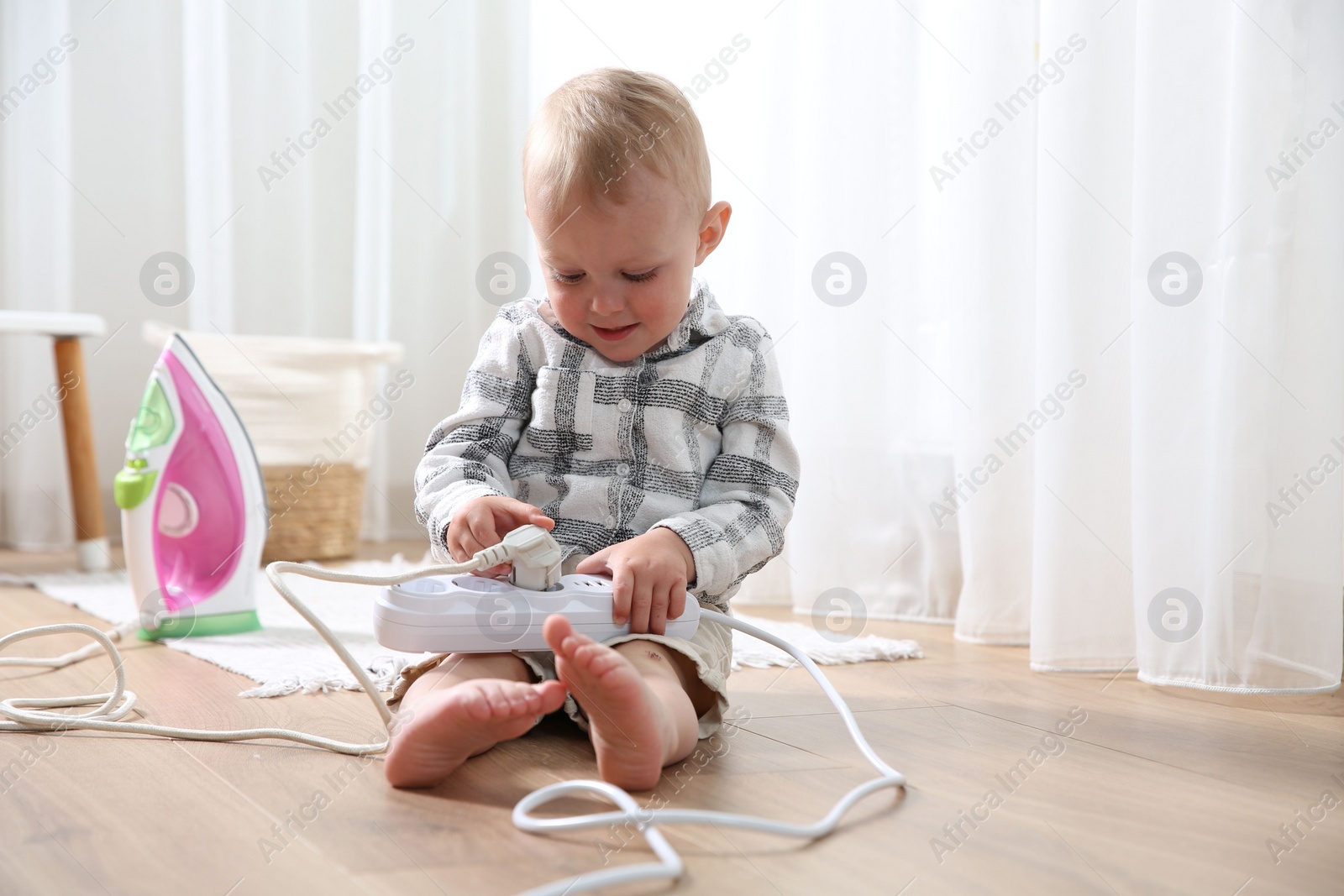 Photo of Little child playing with power strip and iron plug on floor at home. Dangerous situation