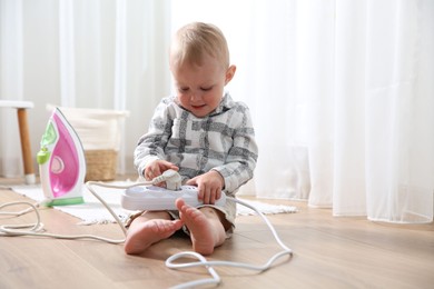 Photo of Little child playing with power strip and iron plug on floor at home. Dangerous situation