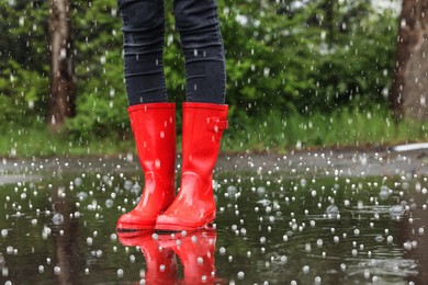 Image of Woman wearing red rubber boots outdoors on rainy day with hail, closeup 