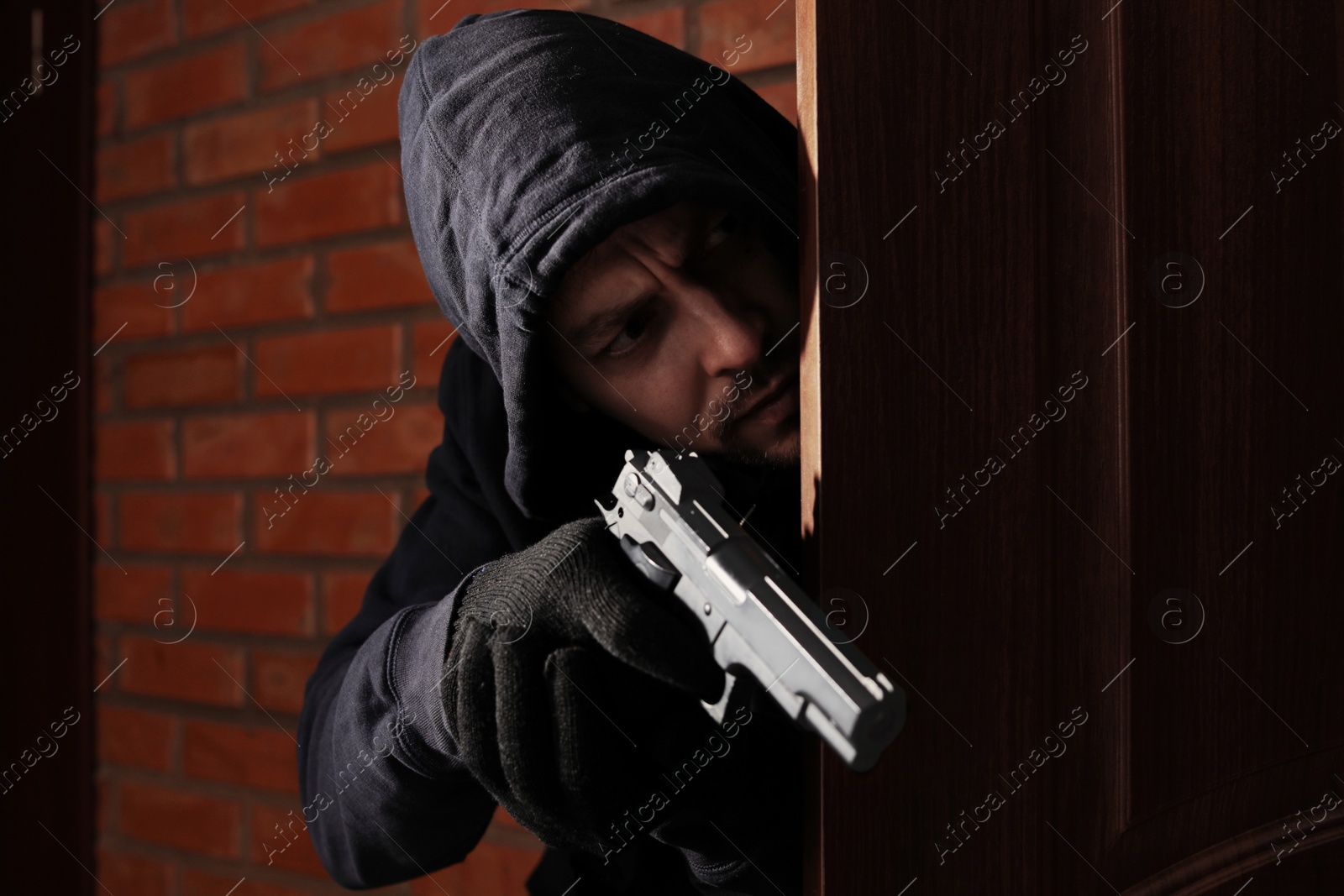 Photo of Man with gun spying behind open door indoors. Criminal offence