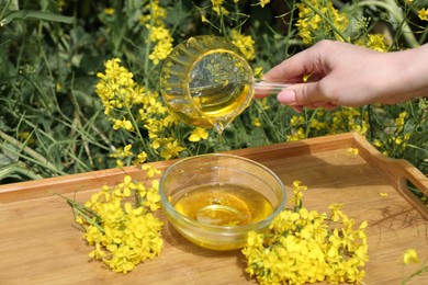 Photo of Woman pouring rapeseed oil from jug into bowl at tray outdoors, closeup