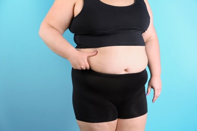 Overweight woman touching belly fat before weight loss on color background