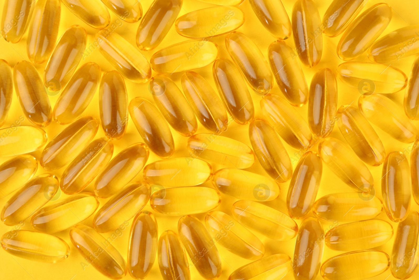 Photo of Many vitamin capsules on yellow background, top view