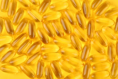 Photo of Many vitamin capsules on yellow background, top view