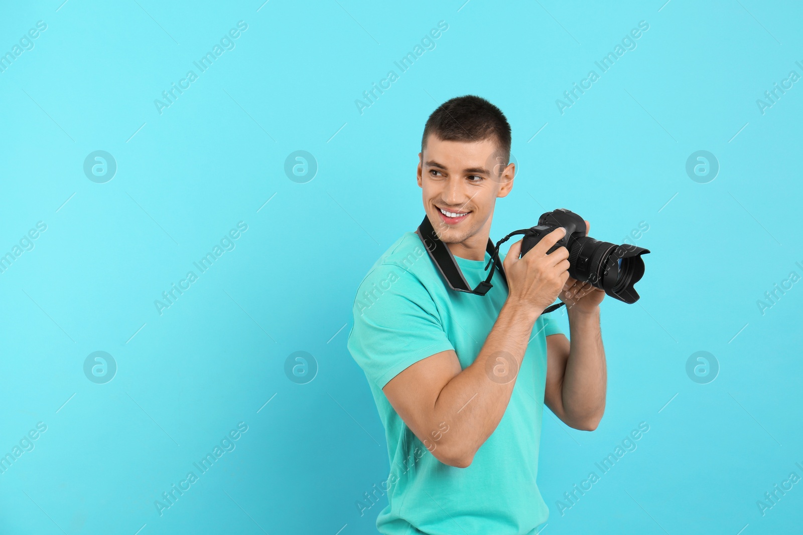 Photo of Young photographer with professional camera on light blue background. Space for text