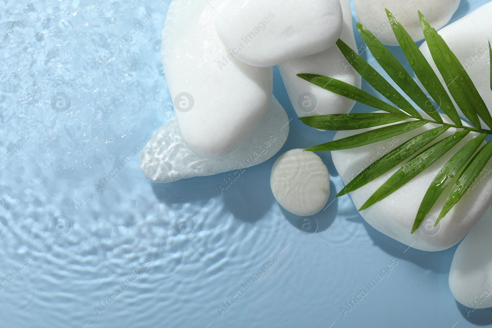 Photo of Spa stones and palm leaf in water on light blue background, flat lay. Space for text