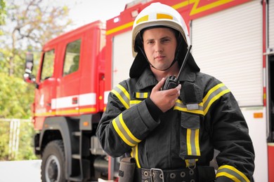 Photo of Portrait of firefighter in uniform with portable radio set near fire truck outdoors