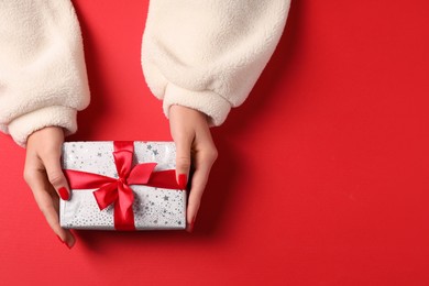 Photo of Christmas present. Woman with gift box on red background, top view. Space for text