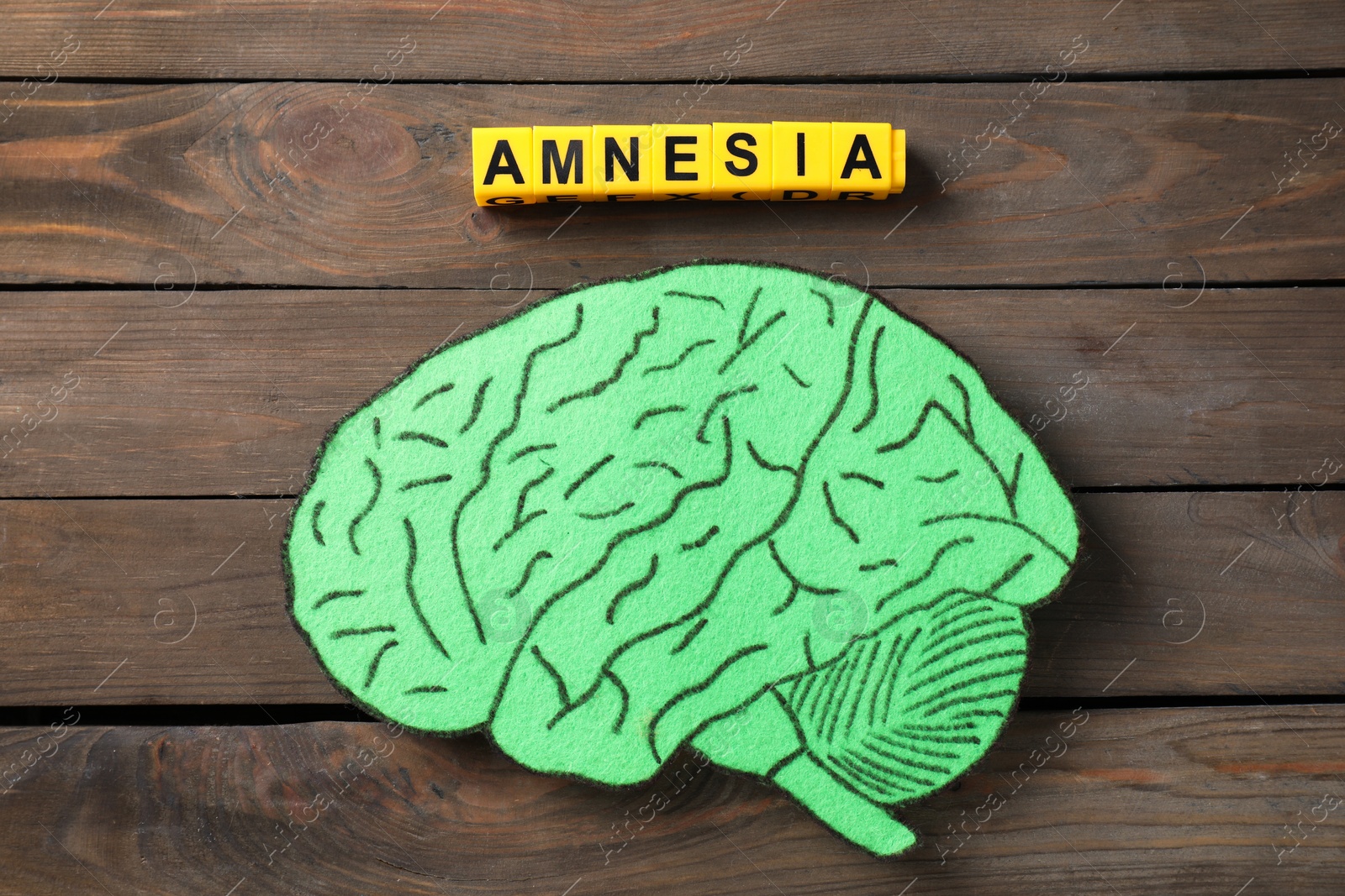 Photo of Yellow cubes with word Amnesia and paper cutout of human brain on wooden table, top view