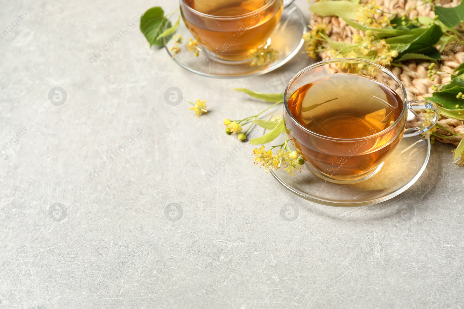 Photo of Tasty tea and linden blossom on light grey table. Space for text