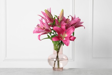 Photo of Beautiful pink lily flowers in vase on light grey table against white wall