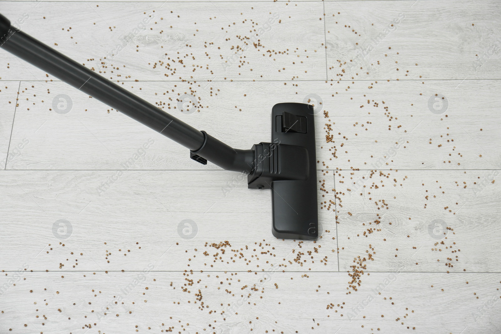 Photo of Removing groats from wooden floor with vacuum cleaner at home, top view