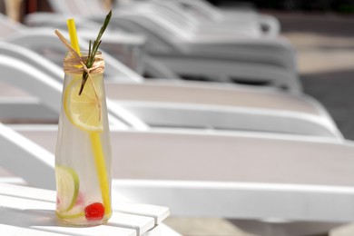 Photo of Refreshing tasty lemonade served in glass bottle on white deck chair. Space for text