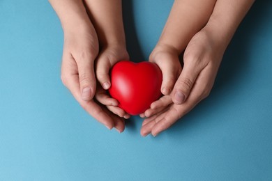Photo of Mother and her child holding red decorative heart on light blue background, top view