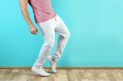 Photo of Young man in stylish jeans near color wall, focus on legs