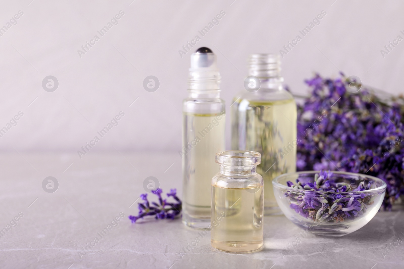 Photo of Bottles of essential oil and bowl with lavender flowers on stone table against light background. Space for text