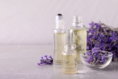 Bottles of essential oil and bowl with lavender flowers on stone table against light background. Space for text