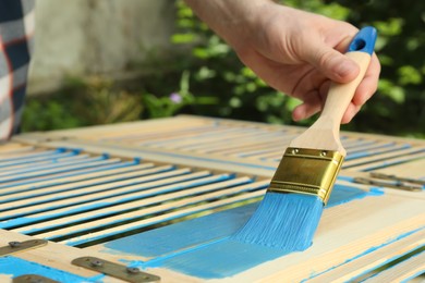 Photo of Man painting wooden surface with blue dye outdoors, closeup. Space for text