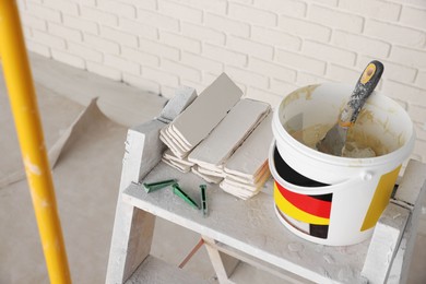 Photo of Bucket with cement, tile spacers and many white decorative bricks in room