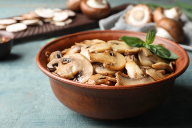 Photo of Delicious cooked mushrooms with basil in bowl on table