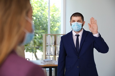 Photo of Man in protective face mask saying hello in office. Keeping social distance during coronavirus pandemic