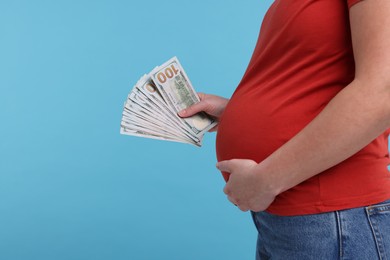 Photo of Surrogate mother. Pregnant woman with dollar banknotes on light blue background, closeup. Space for text