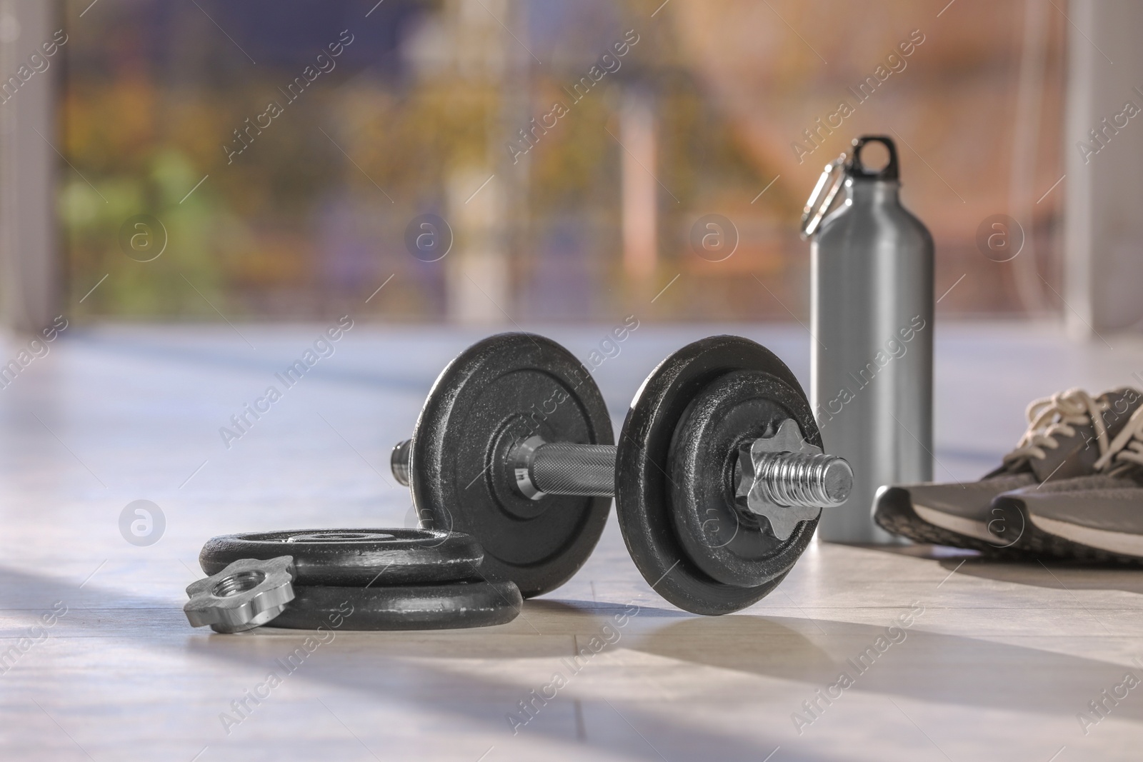 Photo of Adjustable dumbbell with parts, bottle and sneakers on floor indoors. Space for text