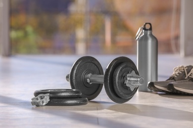 Photo of Adjustable dumbbell with parts, bottle and sneakers on floor indoors. Space for text