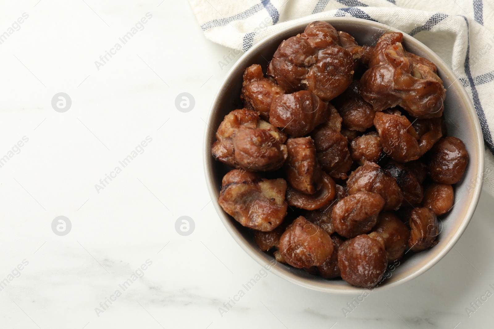 Photo of Roasted edible sweet chestnuts in bowl on white marble table, top view. Space for text