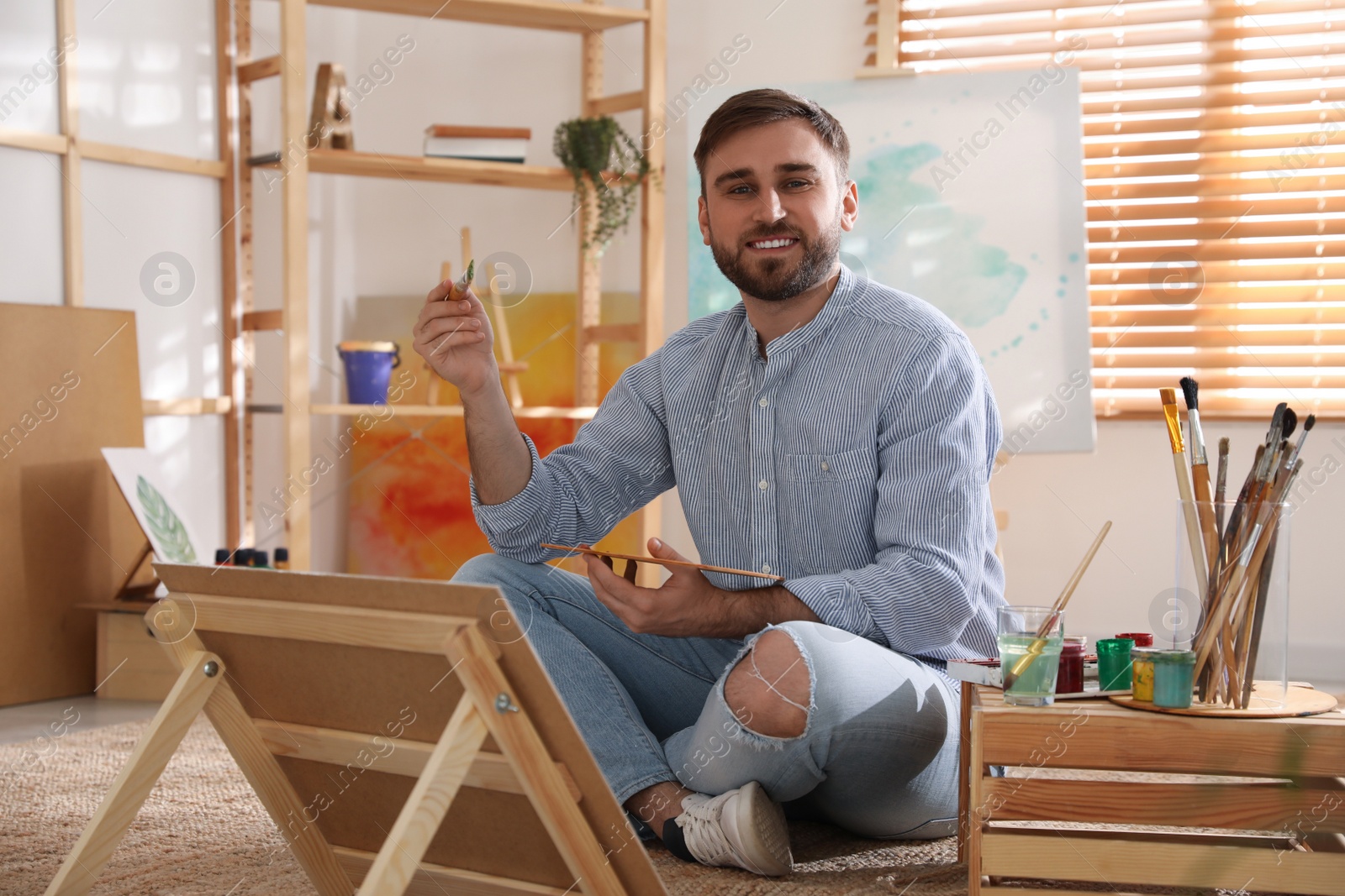 Photo of Young man painting on easel with brush in artist studio