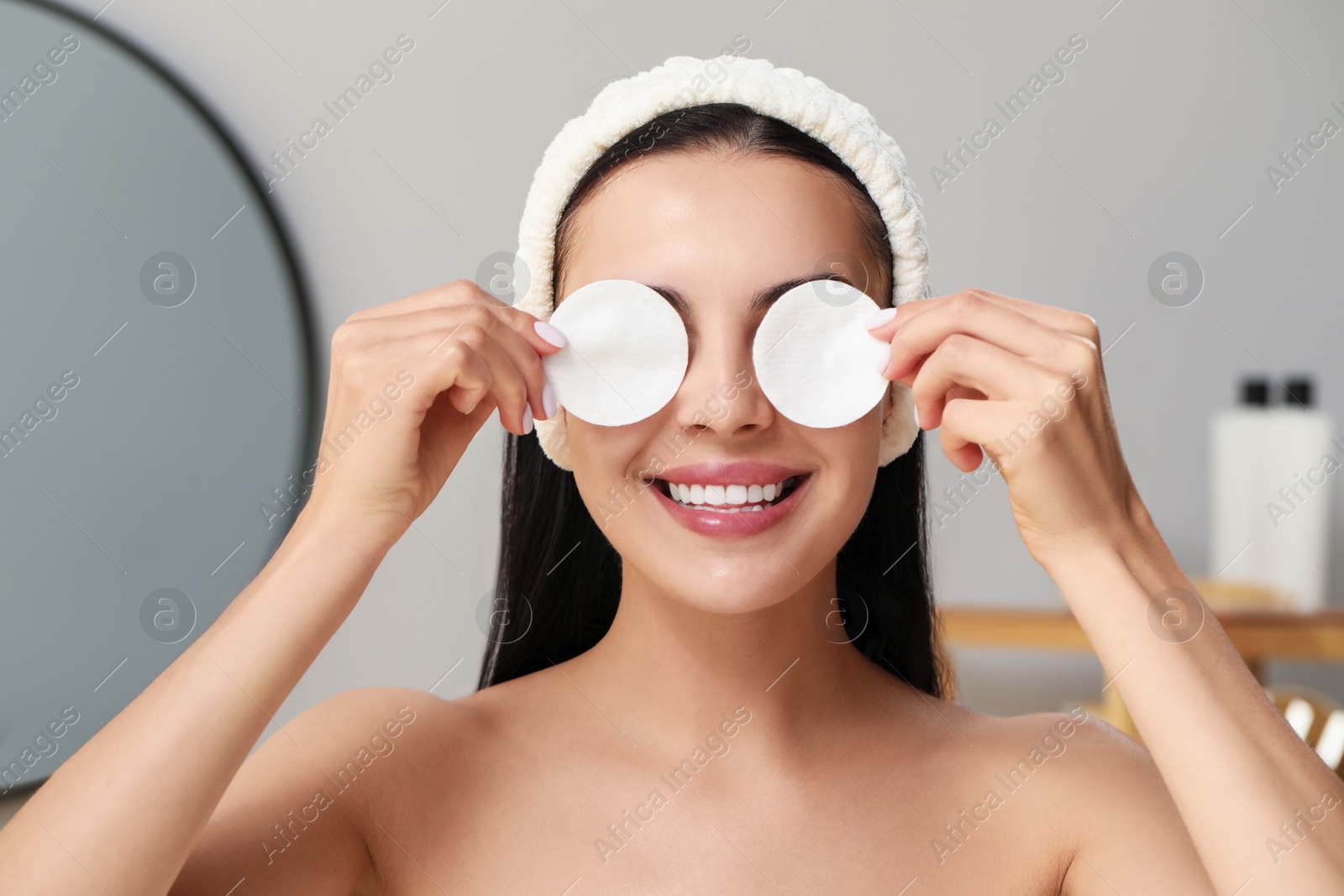 Photo of Young woman using cotton pads with micellar water indoors