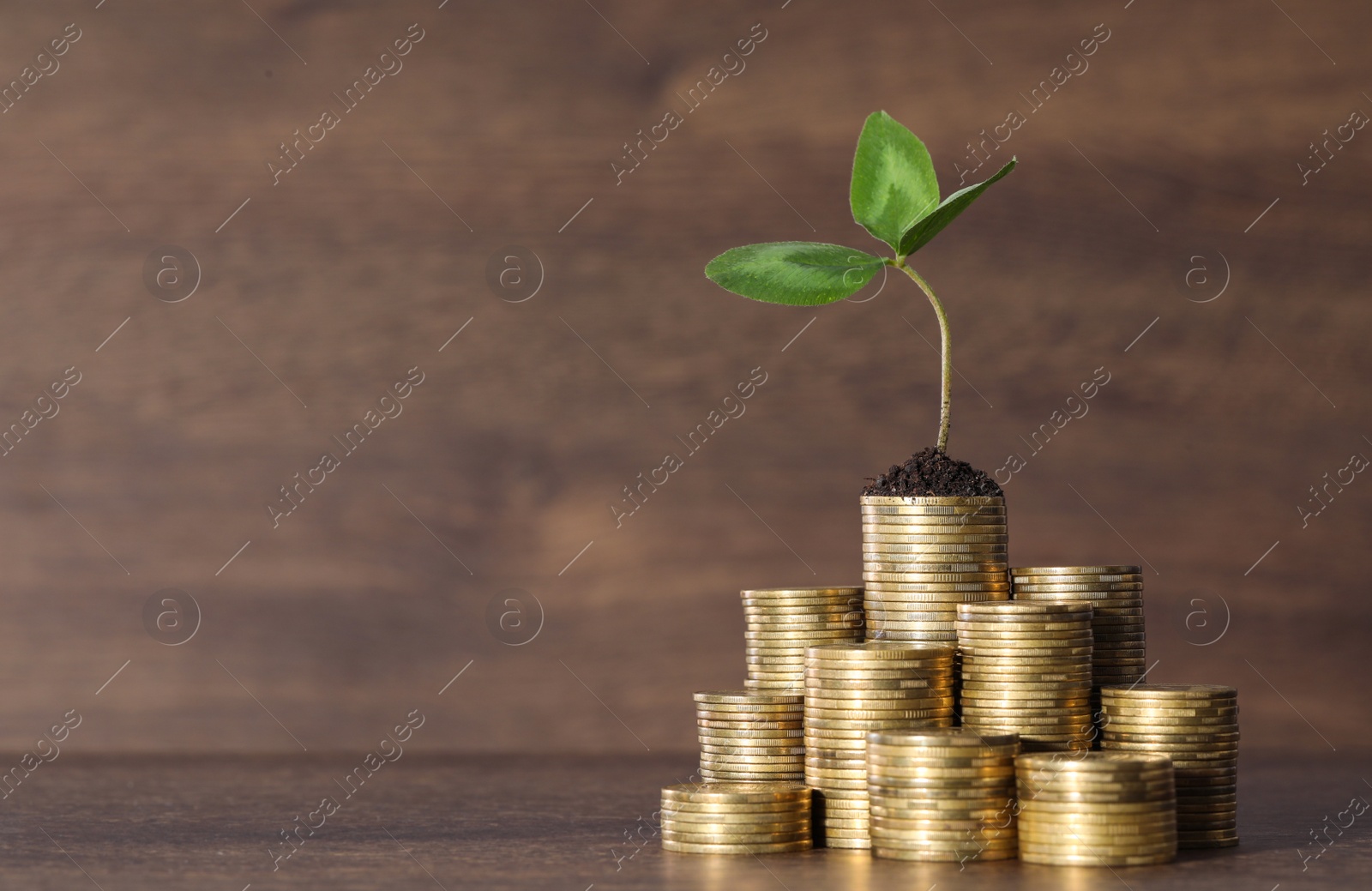Photo of Stacks of coins with green sprout on wooden table, space for text. Investment concept