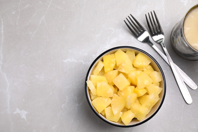 Photo of Tasty canned pineapple pieces and forks on light grey marble table, flat lay. Space for text