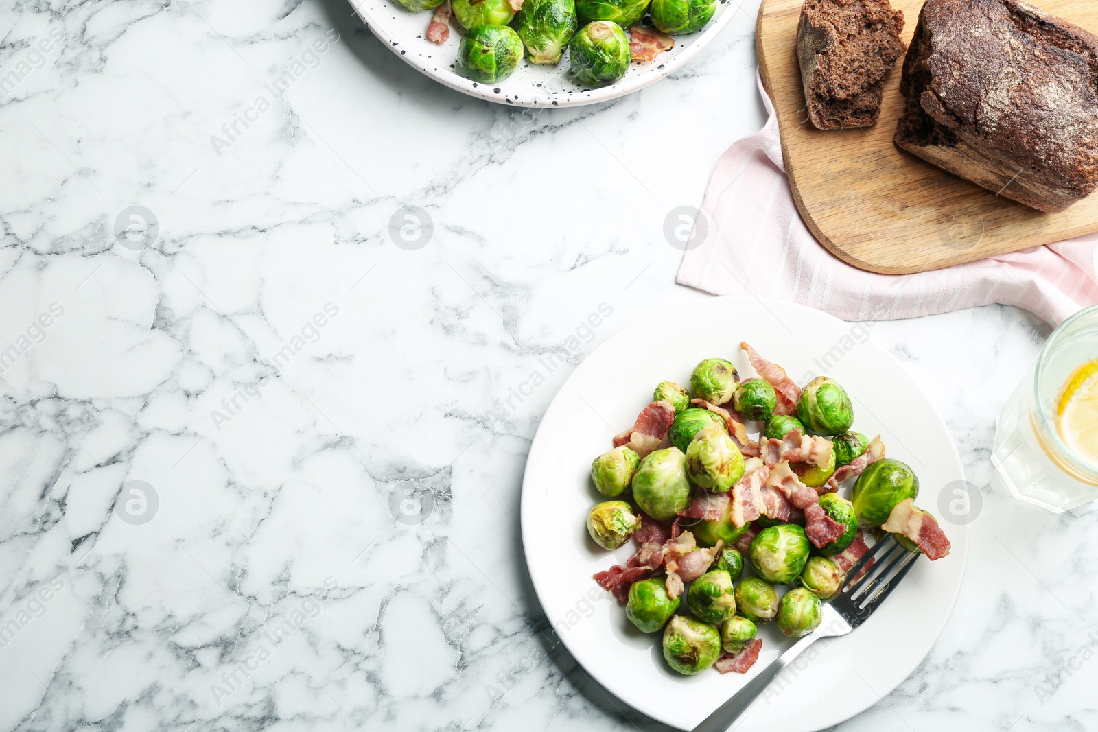 Photo of Delicious Brussels sprouts with bacon on white marble table, flat lay. Space for text