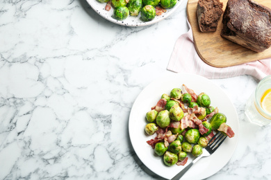 Photo of Delicious Brussels sprouts with bacon on white marble table, flat lay. Space for text