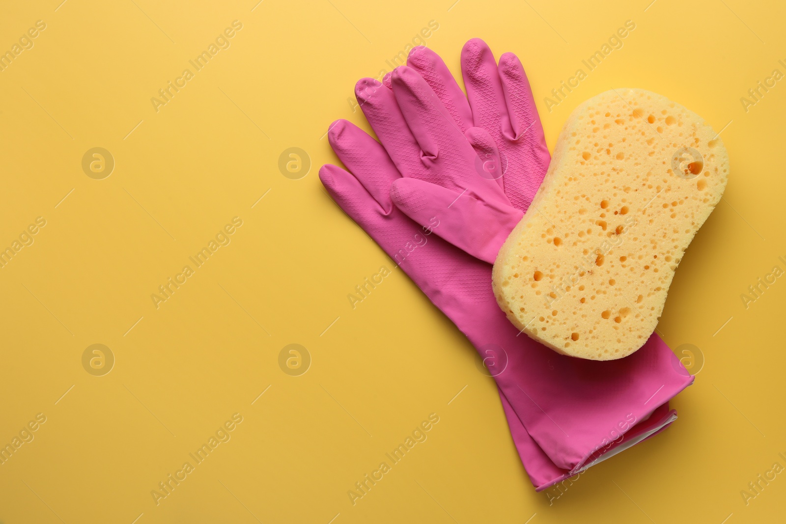 Photo of Sponge and gloves on yellow background, top view. Space for text